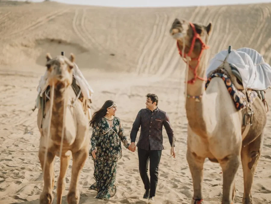 Couple walking hand-in-hand with camels across desert sand dunes in Osian, Rajasthan