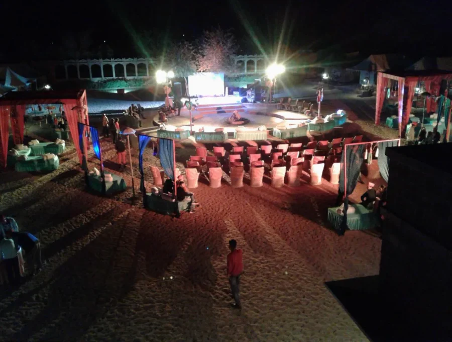 Cultural performance stage with red carpets, lanterns, and seating at desert camp in Osian