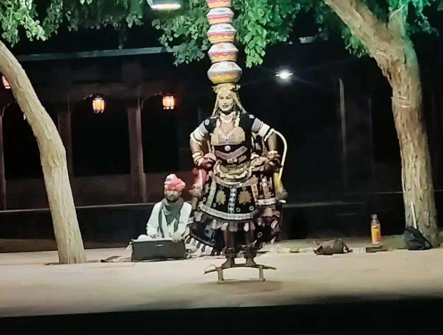 Rajasthani folk dancer balancing stacked brass pots on head with live musicians in Osian